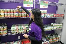 Photo from the New York Times of a woman in a hunter T-shirt grabbing a can of beans off of the shelf. 